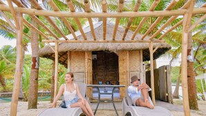A thatched-roof hut with two wicker chairs and a table in front, surrounded by palm trees. - Golden Sands Destination Resorts (Cebu Island)
