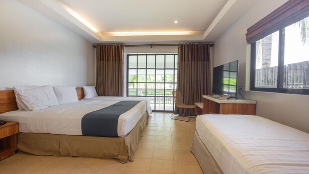 A hotel room with two beds, a desk with a TV, and a window with curtains. - Golden Sands Destination Resorts (Cebu Island)