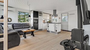 Ein modernes Wohnzimmer mit grauem Sofa, einem Holztisch und einer Küchenzeile mit weißen Schränken und einer Edelstahl-Dunstabzugshaube.