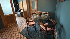 A dining area with a round glass table, four wooden chairs with cushioned seats, a clock on the wall, and a window with curtains. - Istanbul Gem: 3-Bedroom Apartment with Panoramic Terrace and Iconic Sea Views (İstanbul)