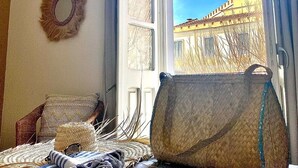 A room with a large window, a wicker chair, a woven bag, and a woven rug. - Fra Cielo e Mare (Cagliari)
