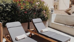 A rooftop terrace with two sun loungers, a potted plant with pink flowers, and a clear view of the surrounding buildings. - Fra Cielo e Mare (Cagliari)