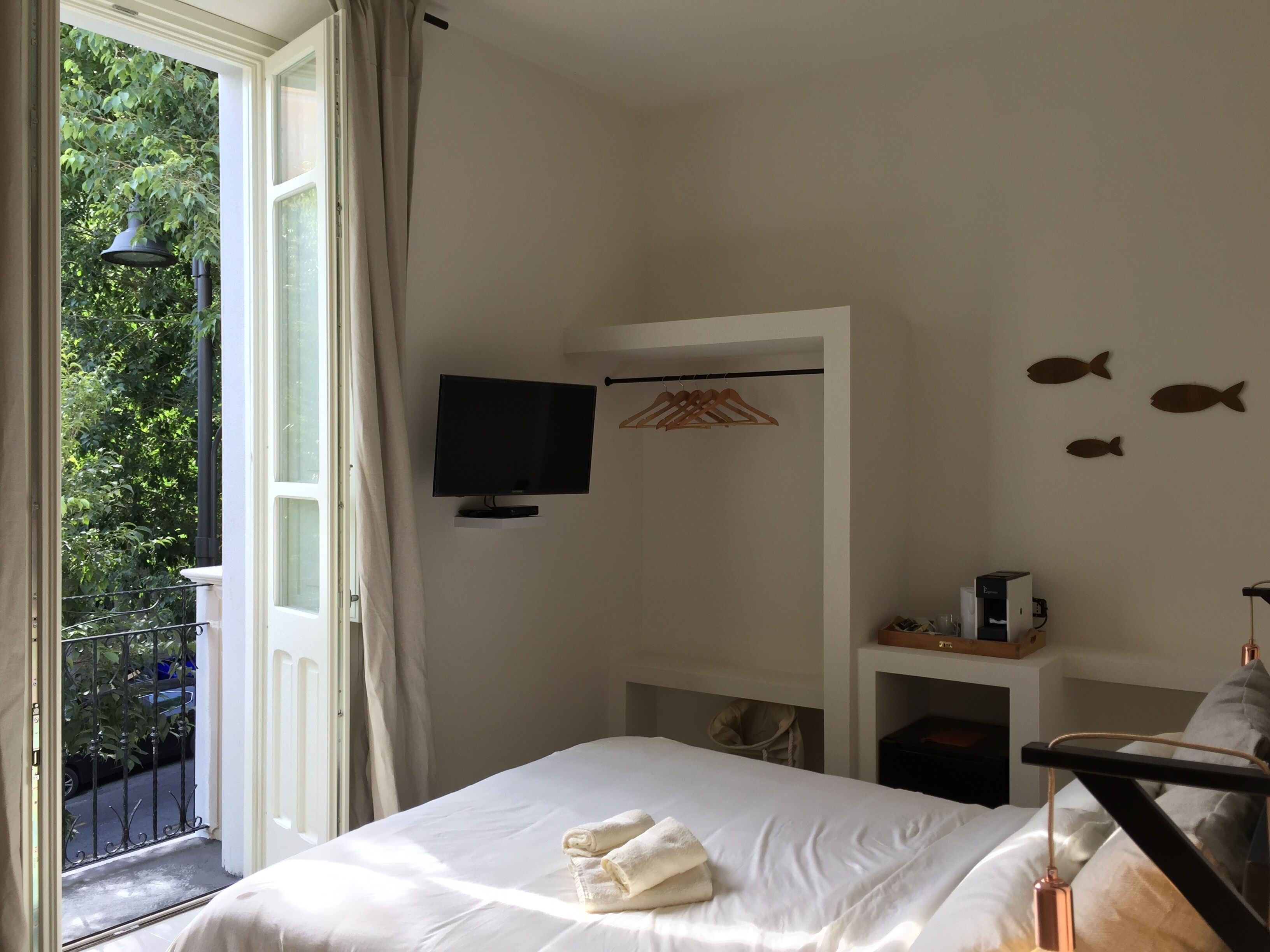 A bedroom with a bed, a television, a small shelf, and a balcony with a view of greenery.