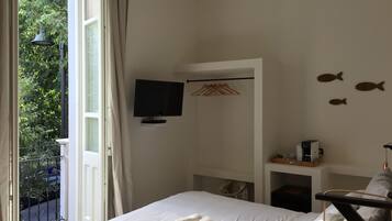 A bedroom with a bed, a television, a small shelf, and a balcony with a view of greenery.