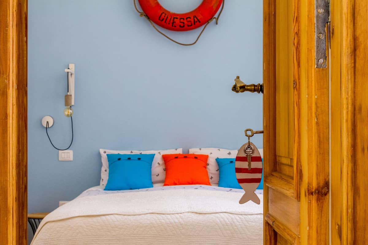 Een slaapkamer met een bed, kussens, een lichtschakelaar op de muur en een deur met een messing handvat.