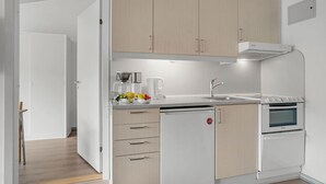 Una cocina compacta con armarios de madera clara, horno empotrado, cafetera y lavabo.