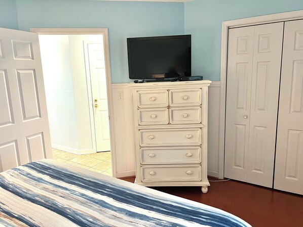 A bedroom with a bed, a dresser, a television on top, and a door.