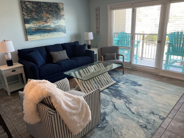 A living room with a dark blue sofa, striped armchairs, a glass coffee table, and a large abstract painting on the wall.