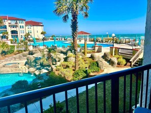 A resort with a pool area, palm trees, and a view of the ocean.