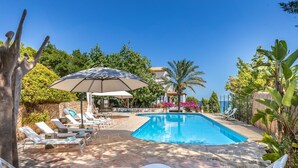 A swimming pool with lounge chairs and umbrellas, surrounded by greenery and a stone patio. - Cavall Bernat 14 - Majorca Villa by the beach (Cala Sant Vicenç)