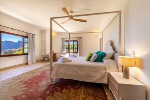 A four-poster bed with a ceiling fan, a bedside table with a lamp, and a view of mountains through the window.