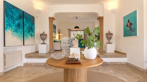 A spacious hallway with a wooden floor, a round table with decorative items, and large abstract paintings on the walls. - Cavall Bernat 14 - Majorca Villa by the beach (Cala Sant Vicenç)