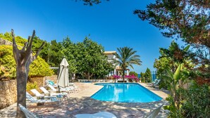 A swimming pool with lounge chairs and umbrellas, surrounded by greenery and a stone wall. - Cavall Bernat - Villa by the sea Majorca (Cala Sant Vicenç)