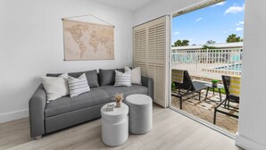 Una sala de estar moderna con un sofá gris, dos mesitas redondas, un mapa del mundo en la pared y vistas a una piscina y una zona de estar al aire libre.
