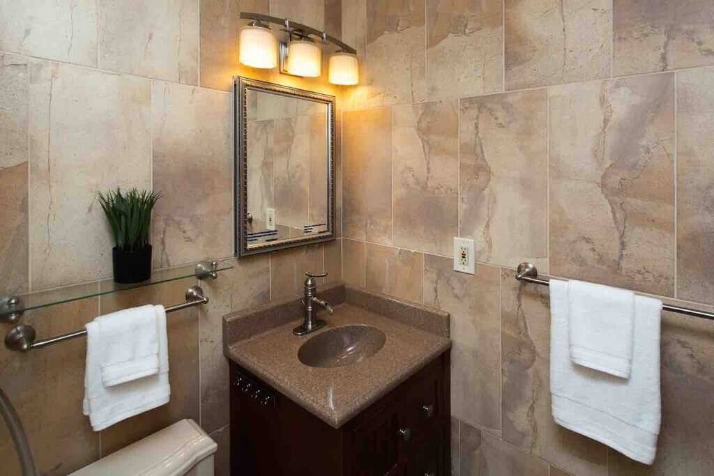 Un baño con lavamanos de granito, un espejo con iluminación y dos toallas en barras.