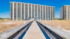 A long wooden boardwalk leading to a high-rise building with multiple balconies. - Phoenix VI 201 | Orange Beach, AL (Orange Beach)