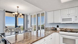 A kitchen with white cabinets, a granite countertop, a microwave, and an oven. There is a view of the ocean through the window. - Phoenix VI 201 | Orange Beach, AL (Orange Beach)