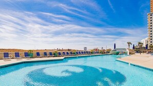 A swimming pool with blue water, surrounded by lounge chairs and a tall building in the background. - Phoenix VI 201 | Orange Beach, AL (Orange Beach)