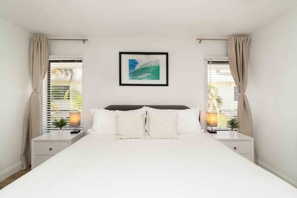 A bedroom with a large bed, two bedside tables, a framed picture on the wall, and curtains on the windows.