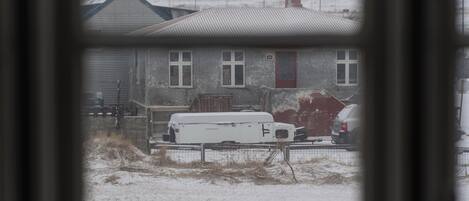 Vista a través de una ventana que muestra una casa con patio nevado, una camioneta blanca estacionada y un coche rojo.