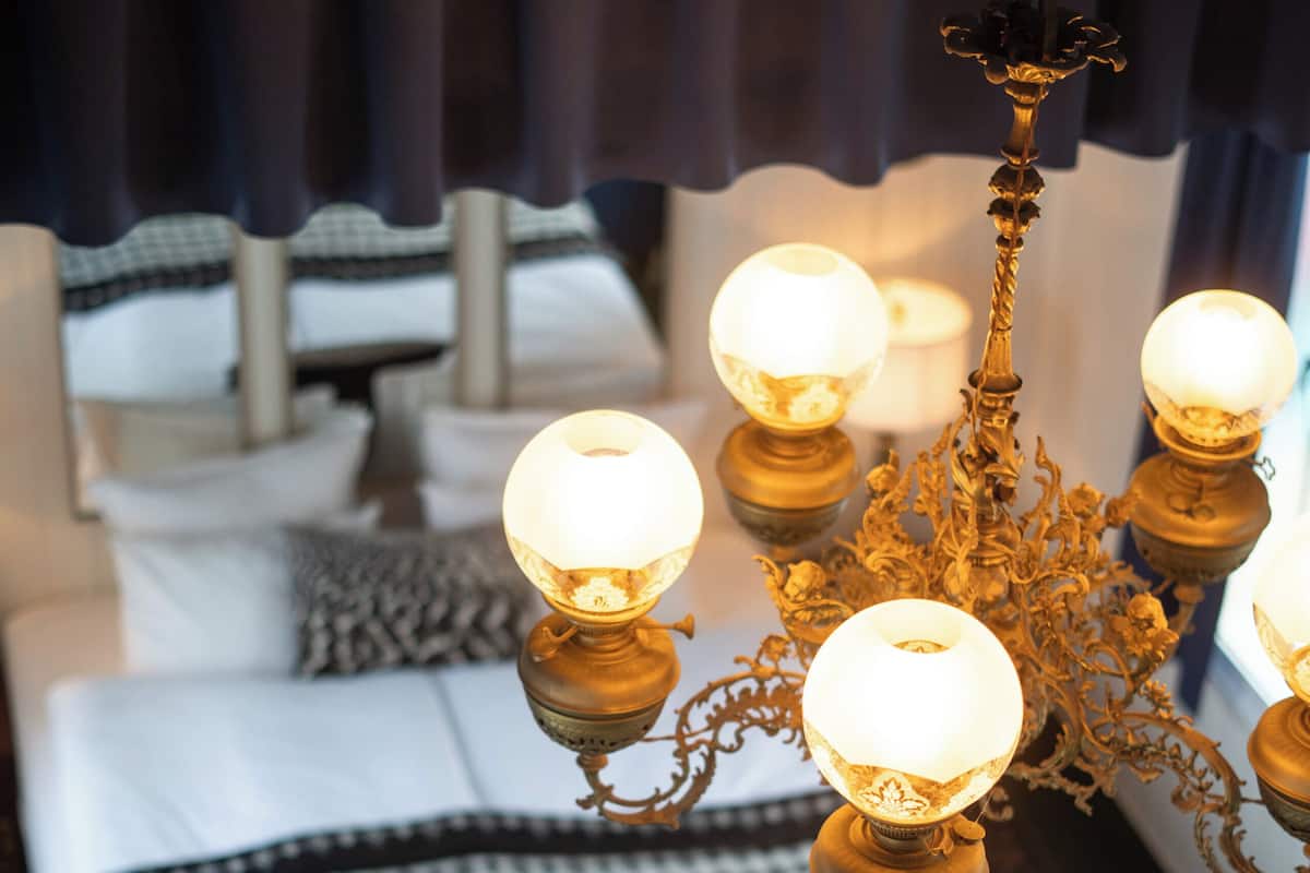 Un candelabro con múltiples luces esféricas en una habitación de hotel con una colcha a cuadros y un ventanal con cortinas.