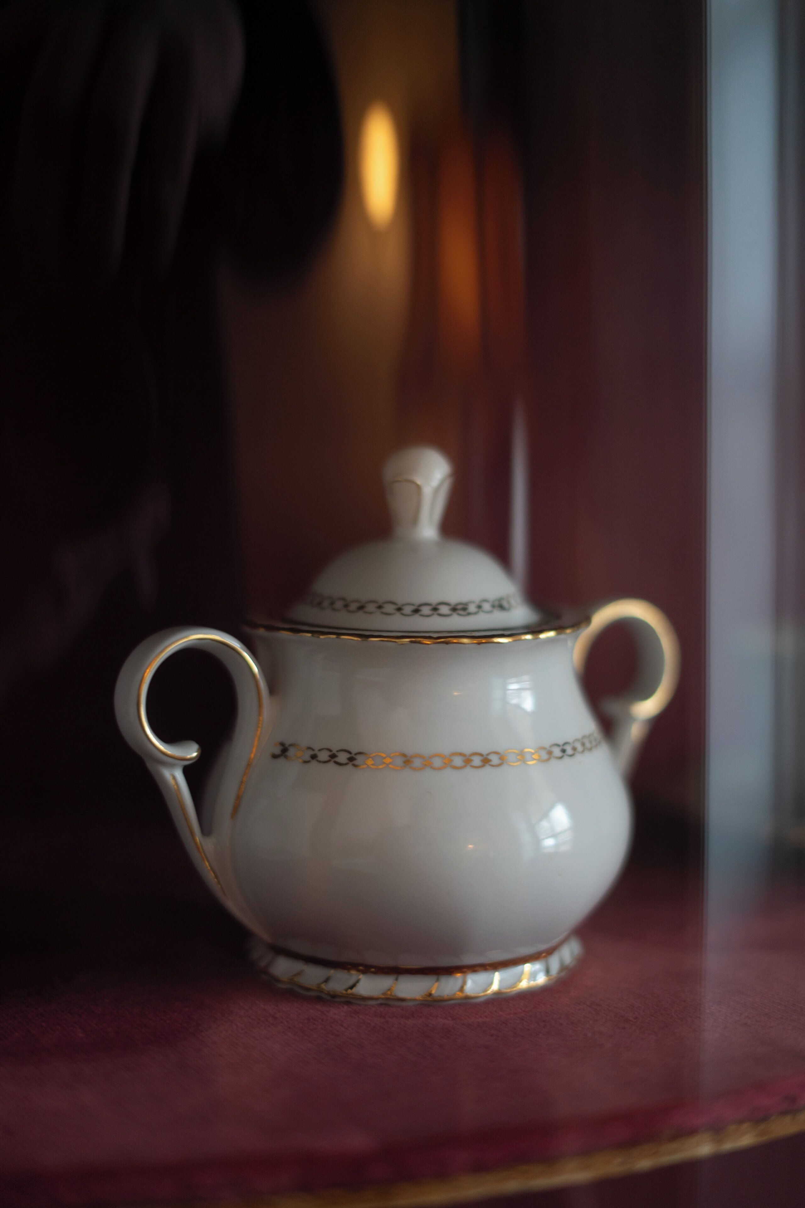 A white ceramic jug with gold trim and handles on a red surface.