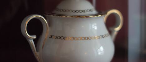 A white ceramic jug with gold trim and handles on a red surface.