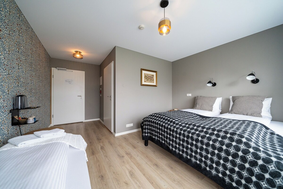 A hotel room with a bed, bedside tables, a wardrobe, a door, and a wall-mounted light fixture.