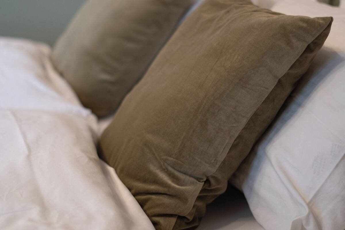 Una cama bien hecha con almohadas color beige y marrón, una almohada blanca y una manta blanca.