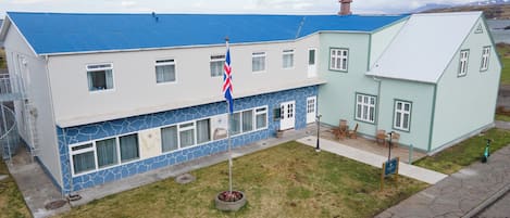 A two-story building with a blue roof, a flagpole with a flag, and a small garden area.