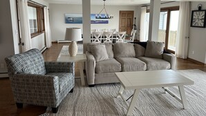 A spacious living room with a large sofa, a patterned armchair, and a white coffee table.