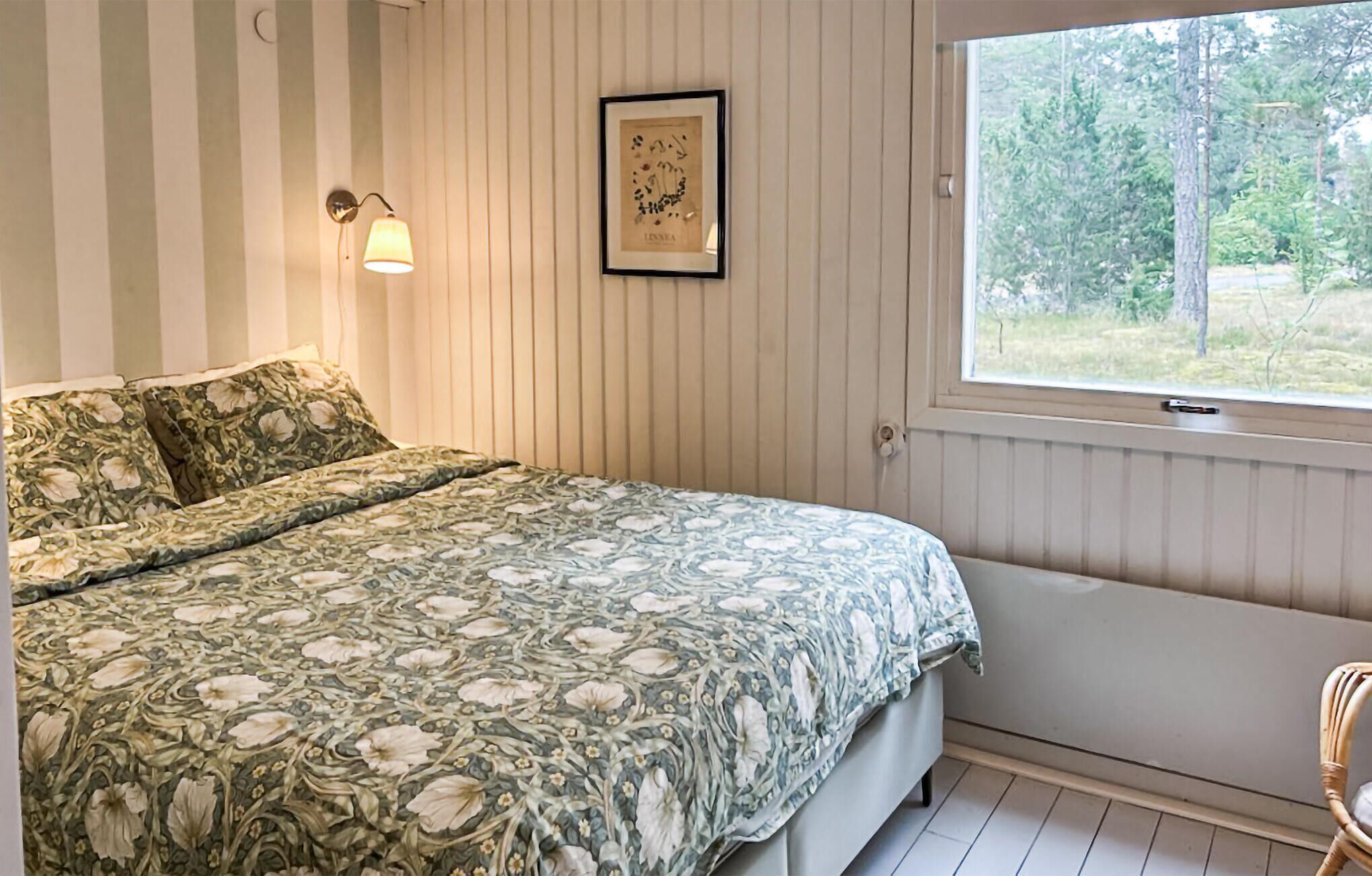 A bedroom with a bed, a window, a wall-mounted lamp, and a framed picture.