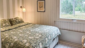 Een slaapkamer met een bed, een raam, een wandlamp en een lijst met een afbeelding.