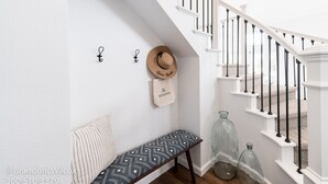 A staircase with white railings and black balusters, a bench with patterned cushions, a hat, and a bag with text on the wall. - Villa Paloma::Private escape with Pool & Hottub (Oceanside)