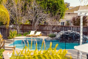 A backyard with a swimming pool, two lounge chairs, a wooden fence, and a house in the background. - Villa Paloma::Private escape with Pool & Hottub (Oceanside)