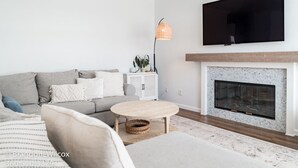 A modern living room with a grey sofa, a round coffee table, a fireplace, and a flat-screen TV mounted above it. - Villa Paloma::Private escape with Pool & Hottub (Oceanside)