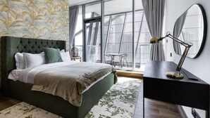 Ein modernes Schlafzimmer mit einem großen Bett, einem Schreibtisch mit Lampe und Blick auf die Stadt durch große Fenster.