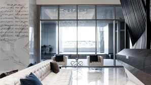 Ein modernes Wohnzimmer mit einem weißen Sofa, zwei Sesseln und einer Glastrennwand.