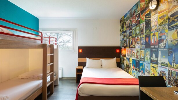 Una habitación con una cama alta, una cama individual, un escritorio y una pared decorada con carteles de viaje.