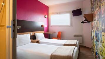 Una habitación de hotel con dos camas, una ventana, un televisor y una pared decorada con carteles.