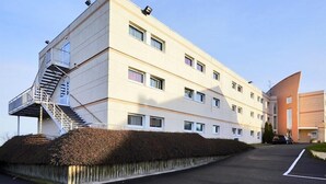 Un edificio de varios pisos con una escalera central, techo plano y zona de estacionamiento.