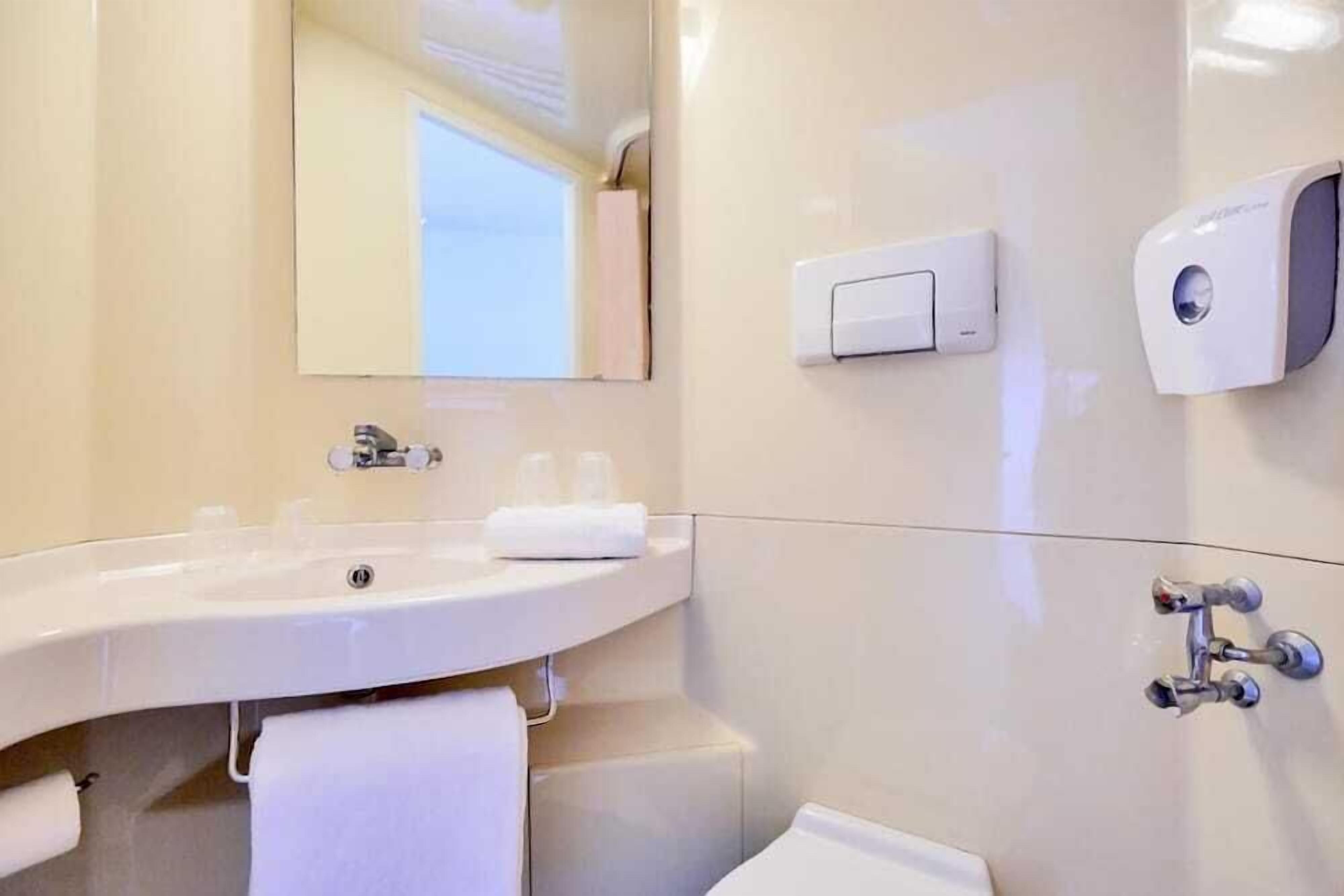 Un baño moderno con lavamanos, espejo, toallero y dispensador de jabón.