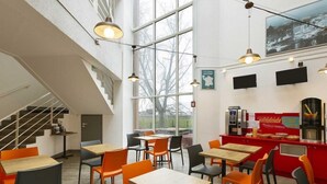 Un café moderno con techos altos, amplios ventanales y una escalera. Mesas y sillas dispuestas para comer.