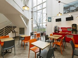 Un café moderno con techos altos, amplios ventanales y una escalera. Mesas y sillas dispuestas para comer.
