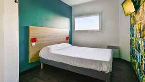 Una cama bien tendida en una habitación con paredes color turquesa, un cabecero de madera, una ventana y una pared decorada con un cartel de colores.