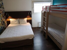 Una cama individual con cabecera de madera y ropa de cama blanca, una litera a la derecha y una pared con un cartel.