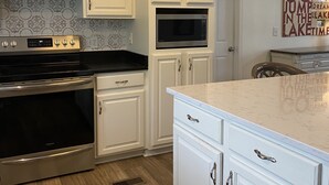 A modern kitchen with white cabinetry, stainless steel appliances, and a marble countertop. - Lake Sinclair retreat with Boat Dock, Waterslide and BIG Views! (Milledgeville)