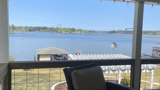 A covered outdoor seating area with a view of a lake, a dock, and a house across the water. - Lake Sinclair retreat with Boat Dock, Waterslide and BIG Views! (Milledgeville)