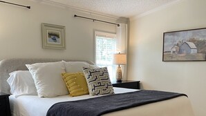 A bedroom with a bed, a nightstand, a lamp, and a window with blinds. - Lake Sinclair retreat with Boat Dock, Waterslide and BIG Views! (Milledgeville)
