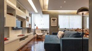 Una sala de estar moderna con un sofá seccional, estanterías empotradas, un televisor de pantalla plana y un comedor con mesa y sillas.